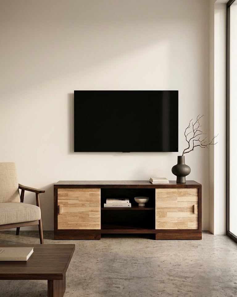 A modern living room scene featuring a dark wood and light oak TV stand console beneath a wall-mounted black television. The room has a warm beige wall, concrete floor, a light beige armchair on the left, and a dark ceramic vase with dried branches on the console.