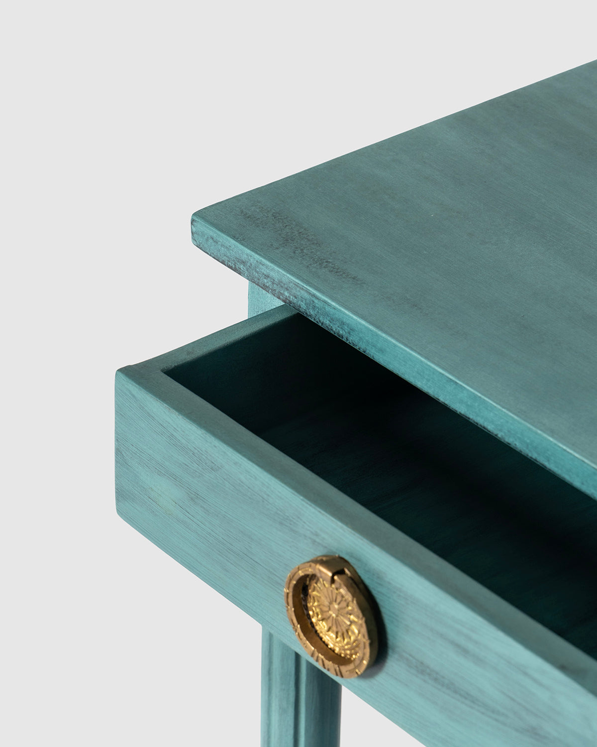 Close-up of a turquoise painted wooden table with an open drawer featuring a round gold pull handle