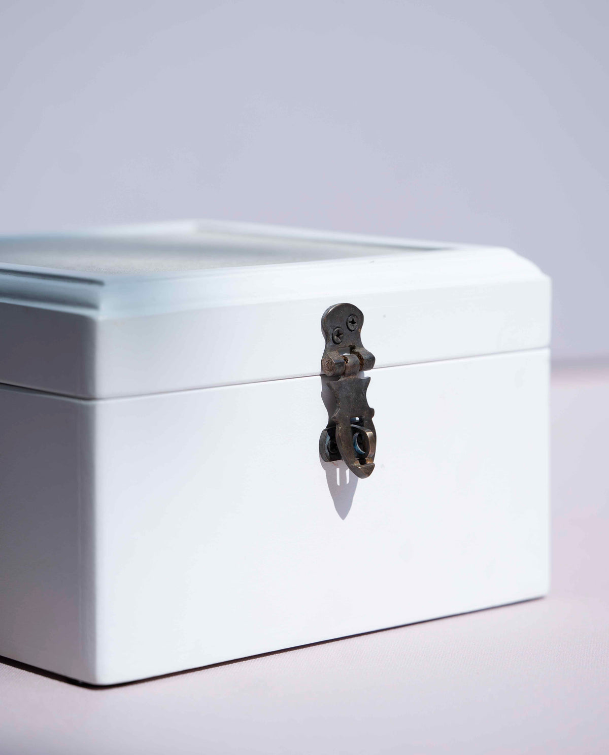 A white painted storage box with a hinged lid and a dark metal decorative latch