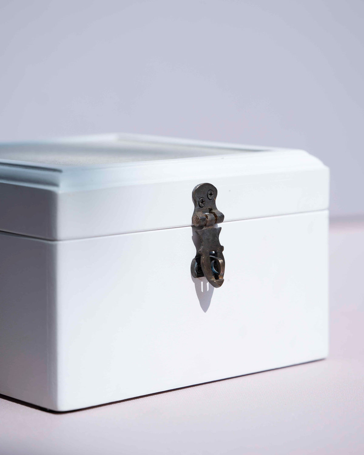 A white painted storage box with a hinged lid and a dark metal decorative latch