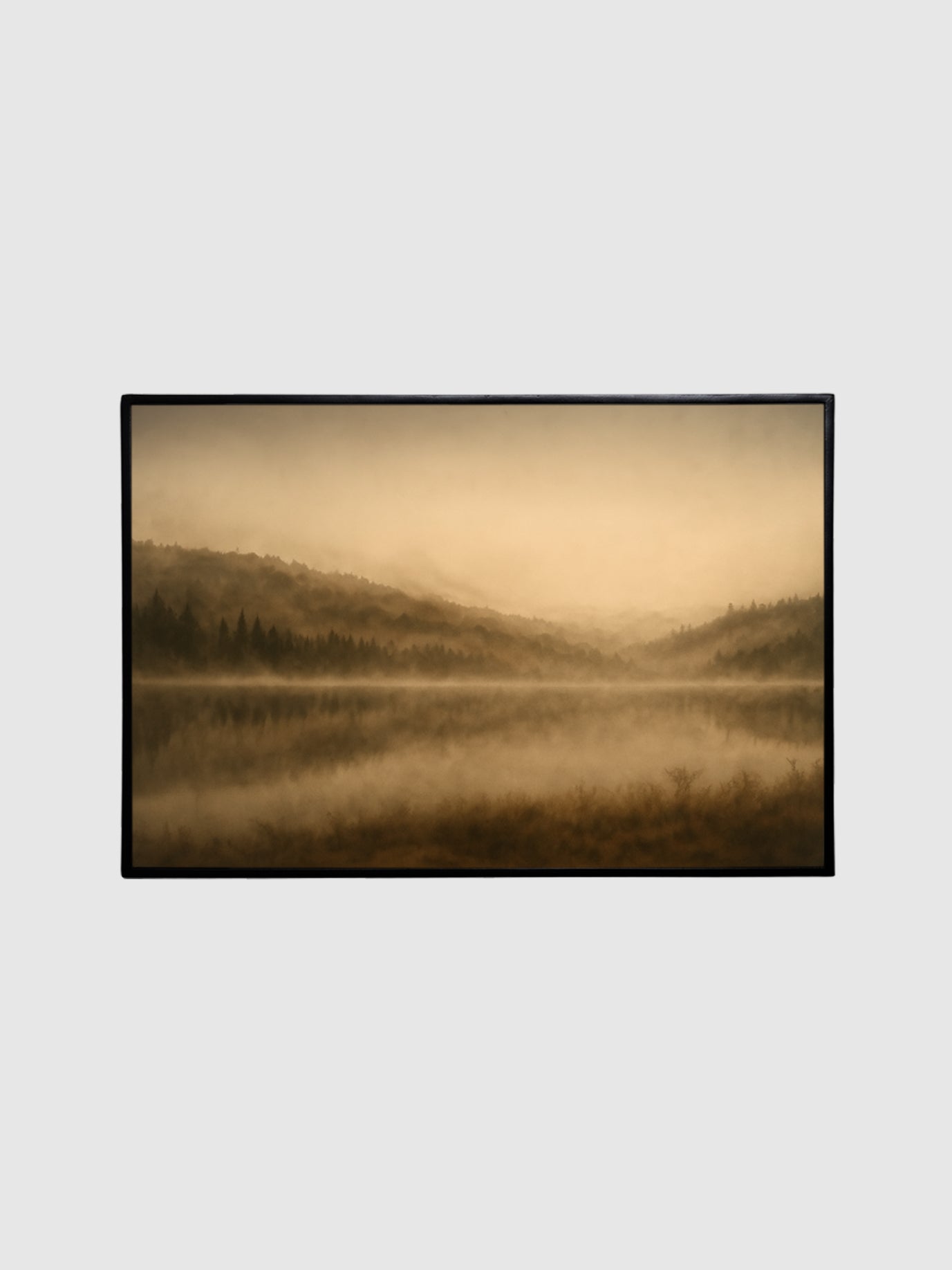 Framed photograph of a misty landscape with hills and a lake on a light gray background