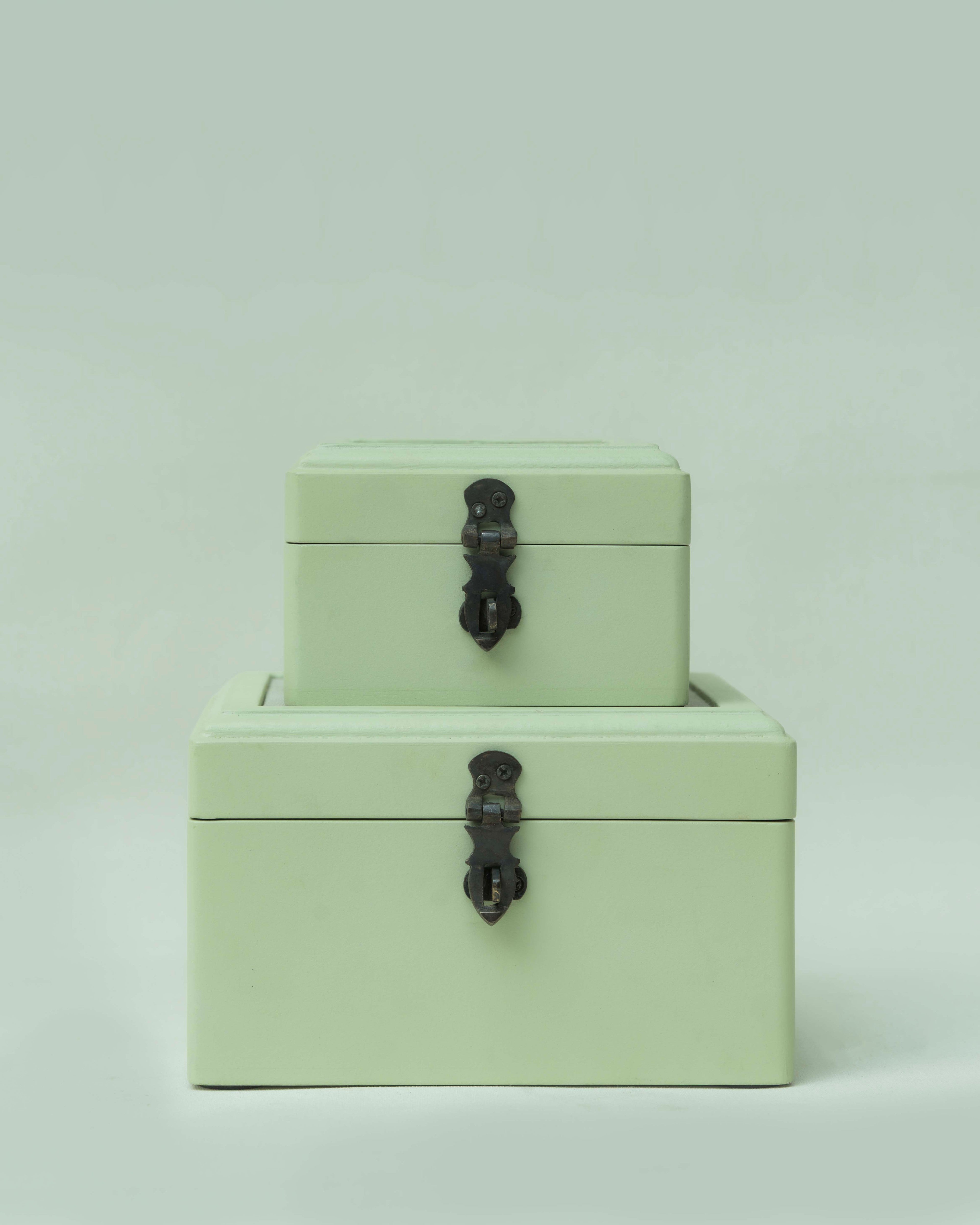 Two stacked rectangular storage boxes in a pale mint green color with dark metal latch closures, set against a solid light gray background.