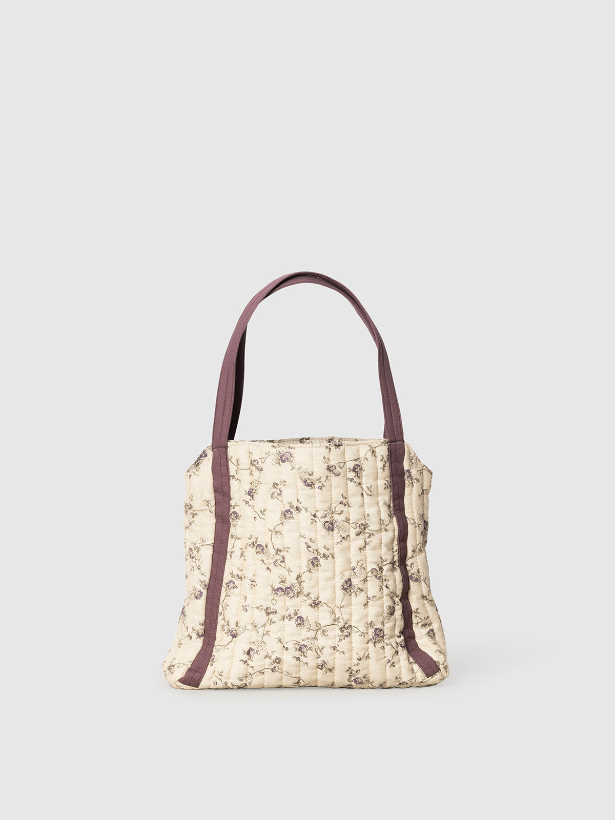 Person holding a floral-patterned tote bag with a purple strap