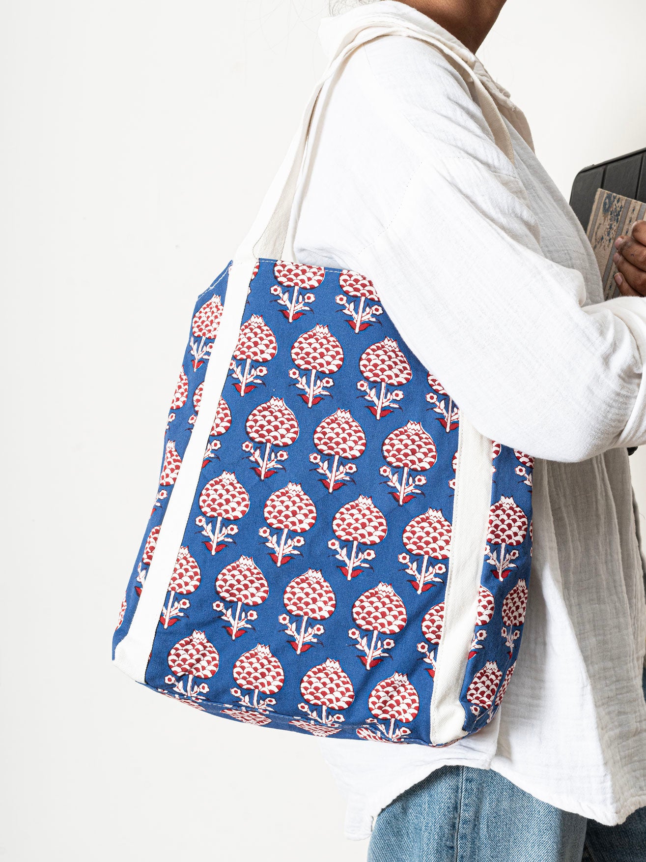 Person holding a blue tote bag with red floral pattern