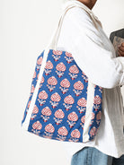 Person holding a blue tote bag with red floral pattern