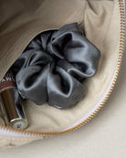 A dark gray satin scrunchie nestled inside a beige fabric zippered pouch