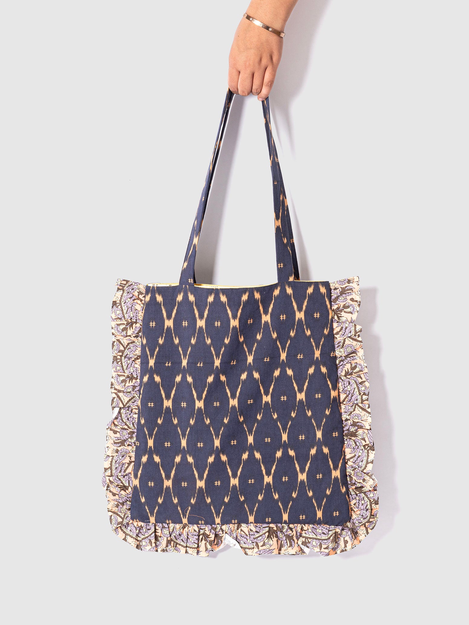 A navy blue tote bag with an ikat print and floral ruffle trim.