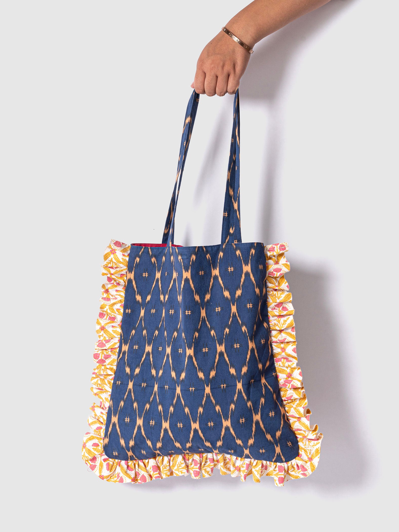 A navy blue tote bag with a mustard-yellow floral ikat print and ruffle detailing on the edges